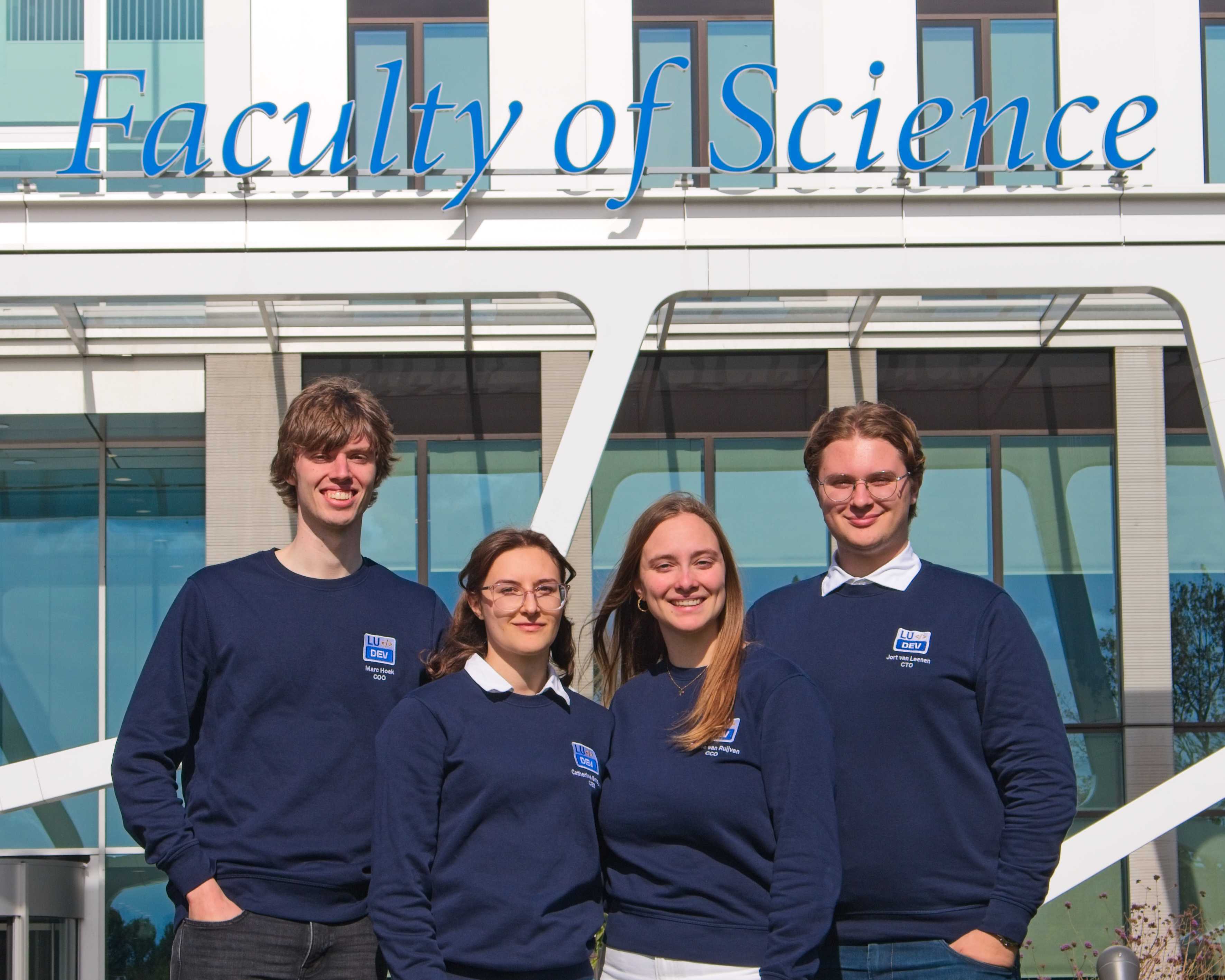 The 2025/2026 LUdev board in front of the Faculty of Science building, wearing navy LUdev sweaters.